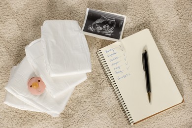 Flat lay composition with baby stuff, list and ultrasound scan on beige carpet