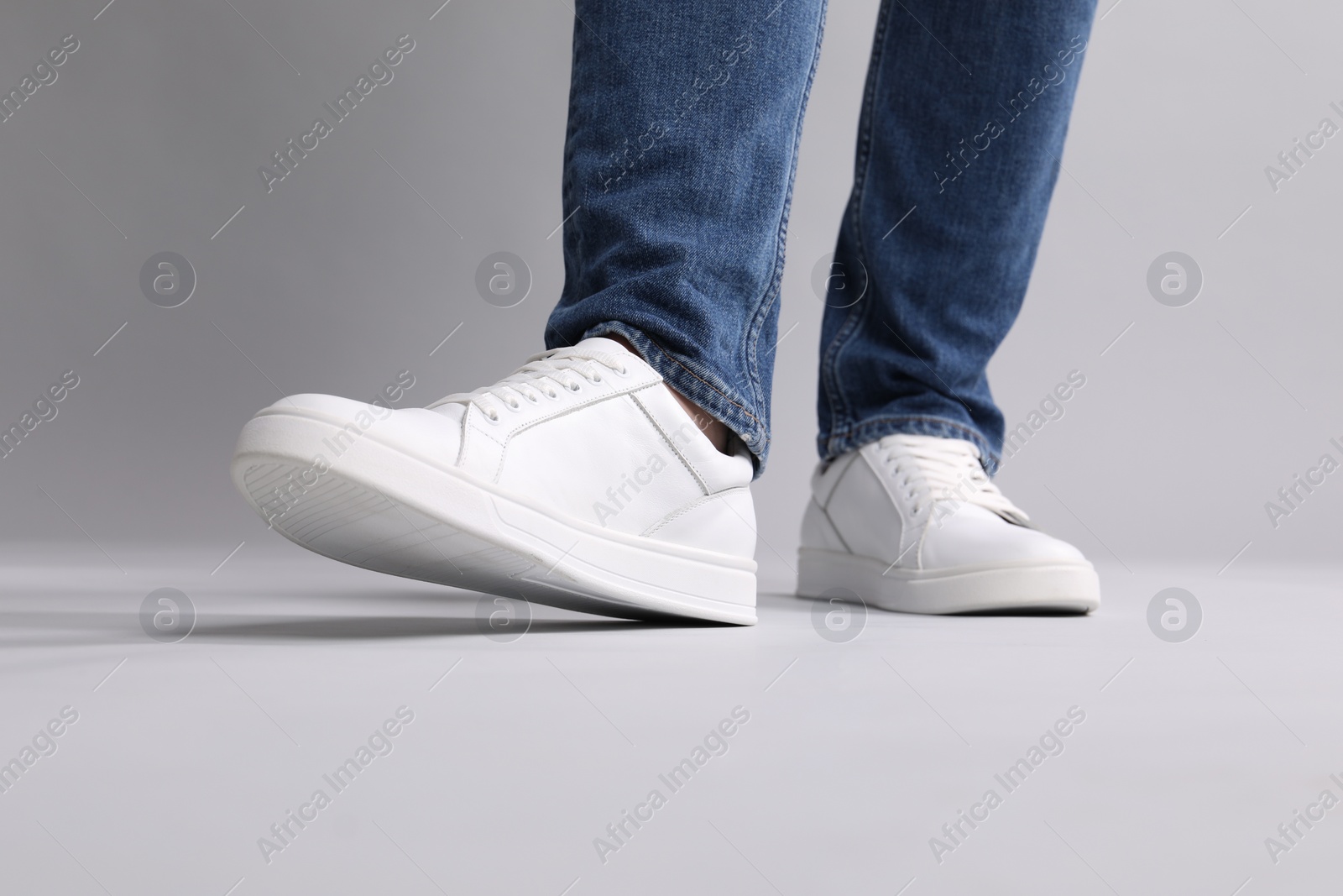 Photo of Man wearing stylish white sneakers on grey background, closeup