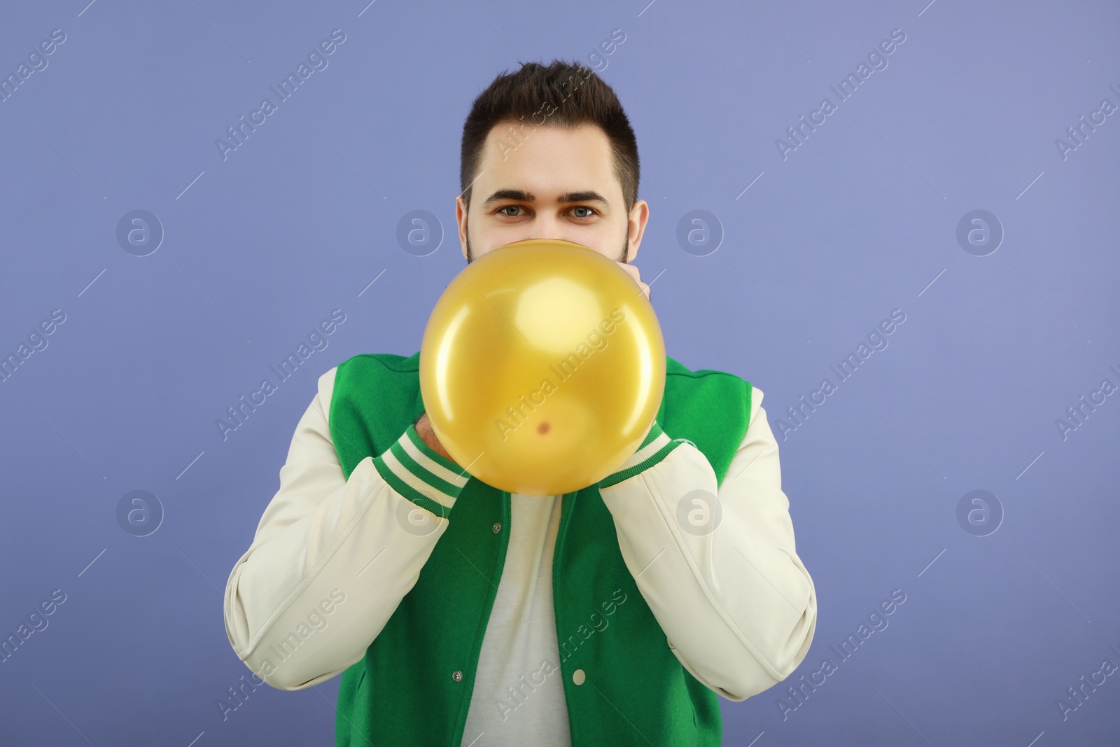 Photo of Man inflating bright balloon on violet background