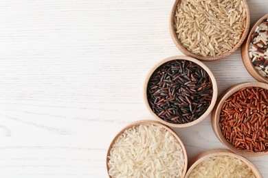 Photo of Flat lay composition with brown and other types of rice in bowls on white wooden background. Space for text