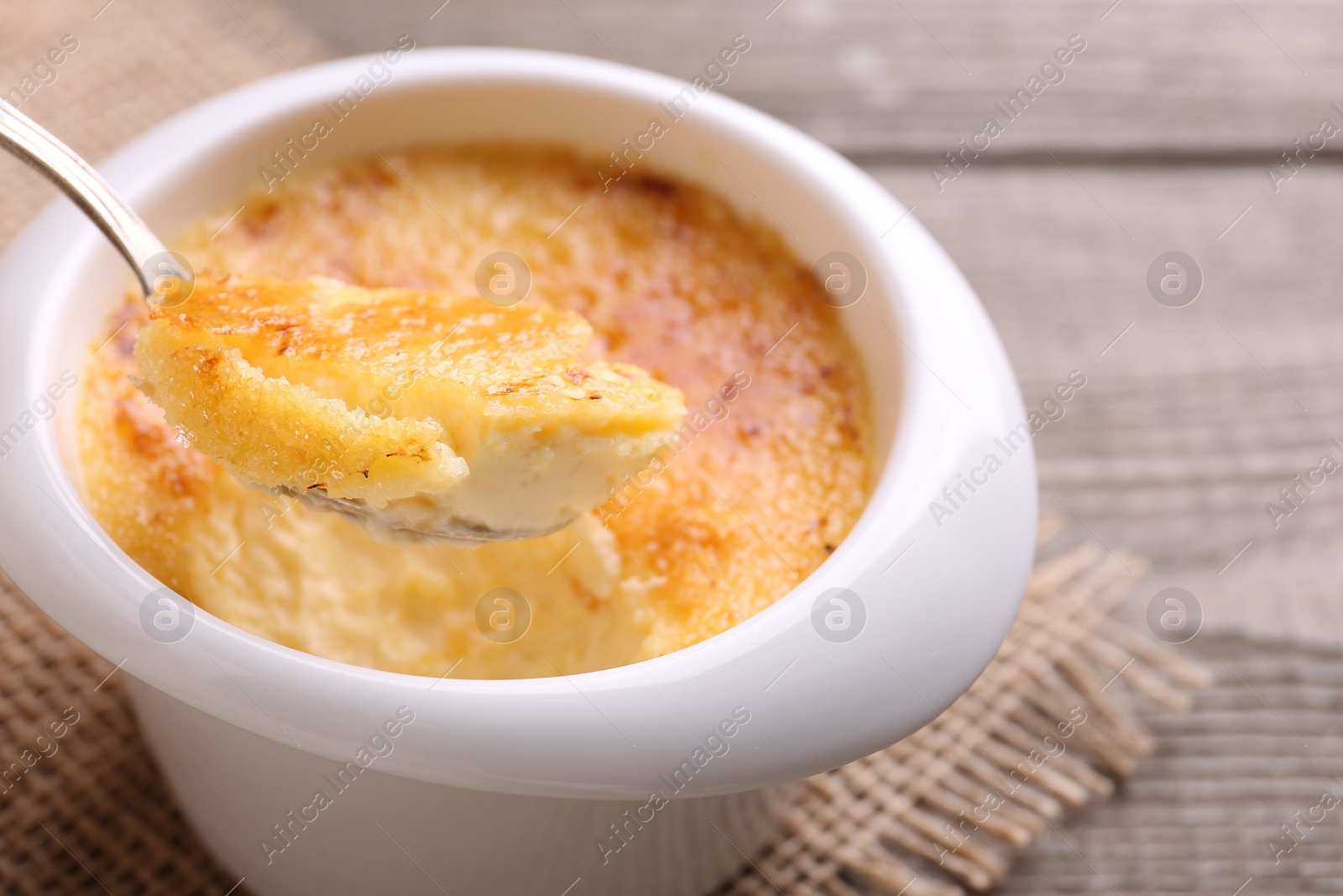 Photo of Taking delicious creme brulee with spoon from bowl at table, closeup