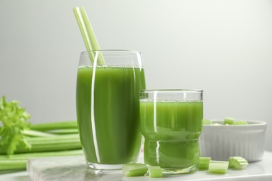 Glasses of delicious celery juice and vegetables on white table