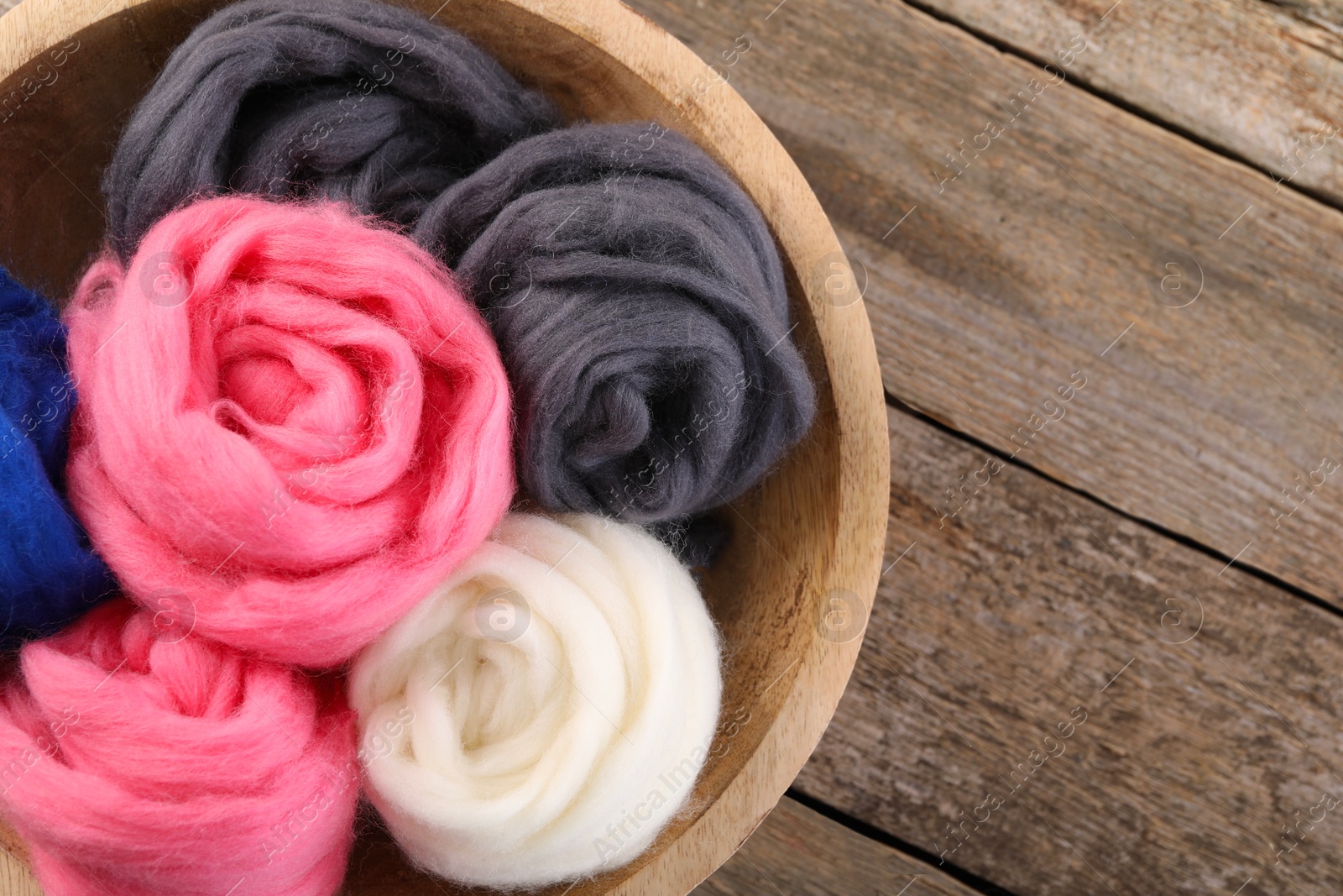 Photo of Colorful felting wool in bowl on wooden table, top view. Space for text