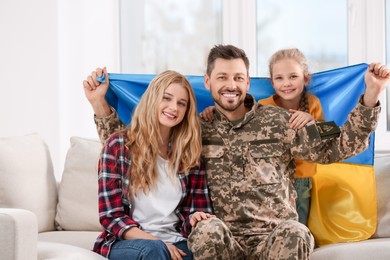 Photo of Soldier in military uniform reunited with his family and Ukrainian flag on sofa at home