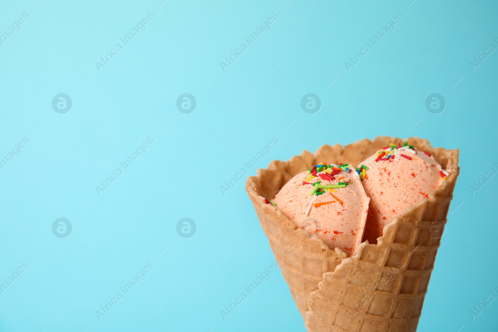 Photo of Delicious ice cream with sprinkles in waffle cone on color background, space for text