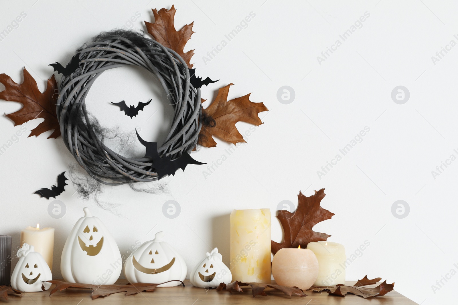 Photo of Different pumpkin shaped holders, autumn leaves and burning candles on wooden table. Halloween decor