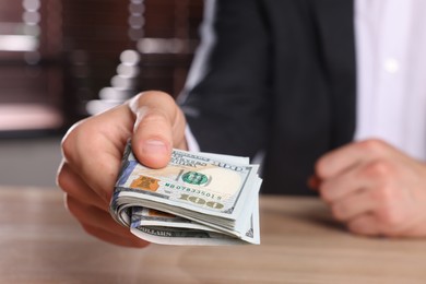 Money exchange. Man holding dollar banknotes at wooden table, closeup