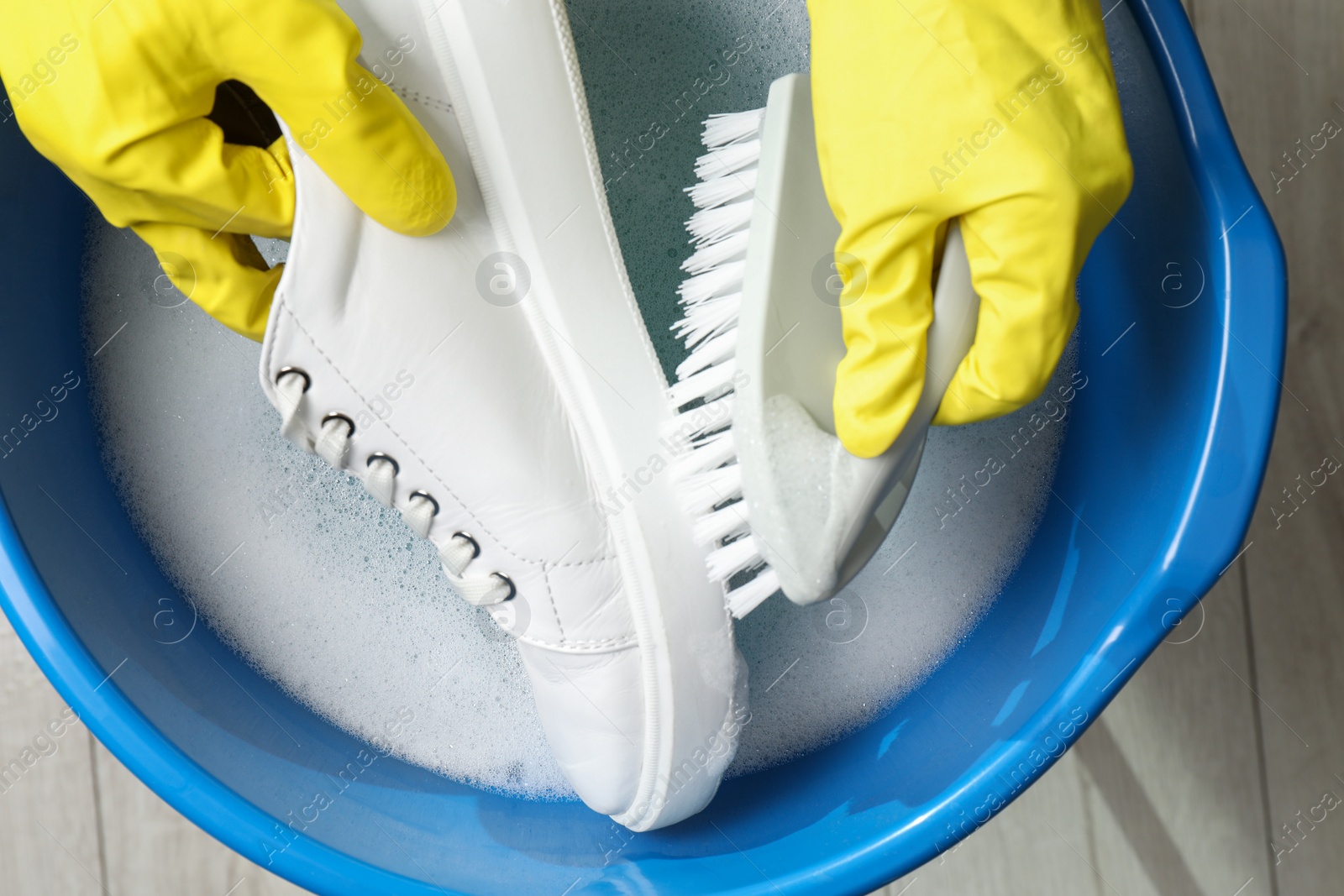 Photo of Woman with gloves and brush cleaning stylish sneakers in wash basin, top view