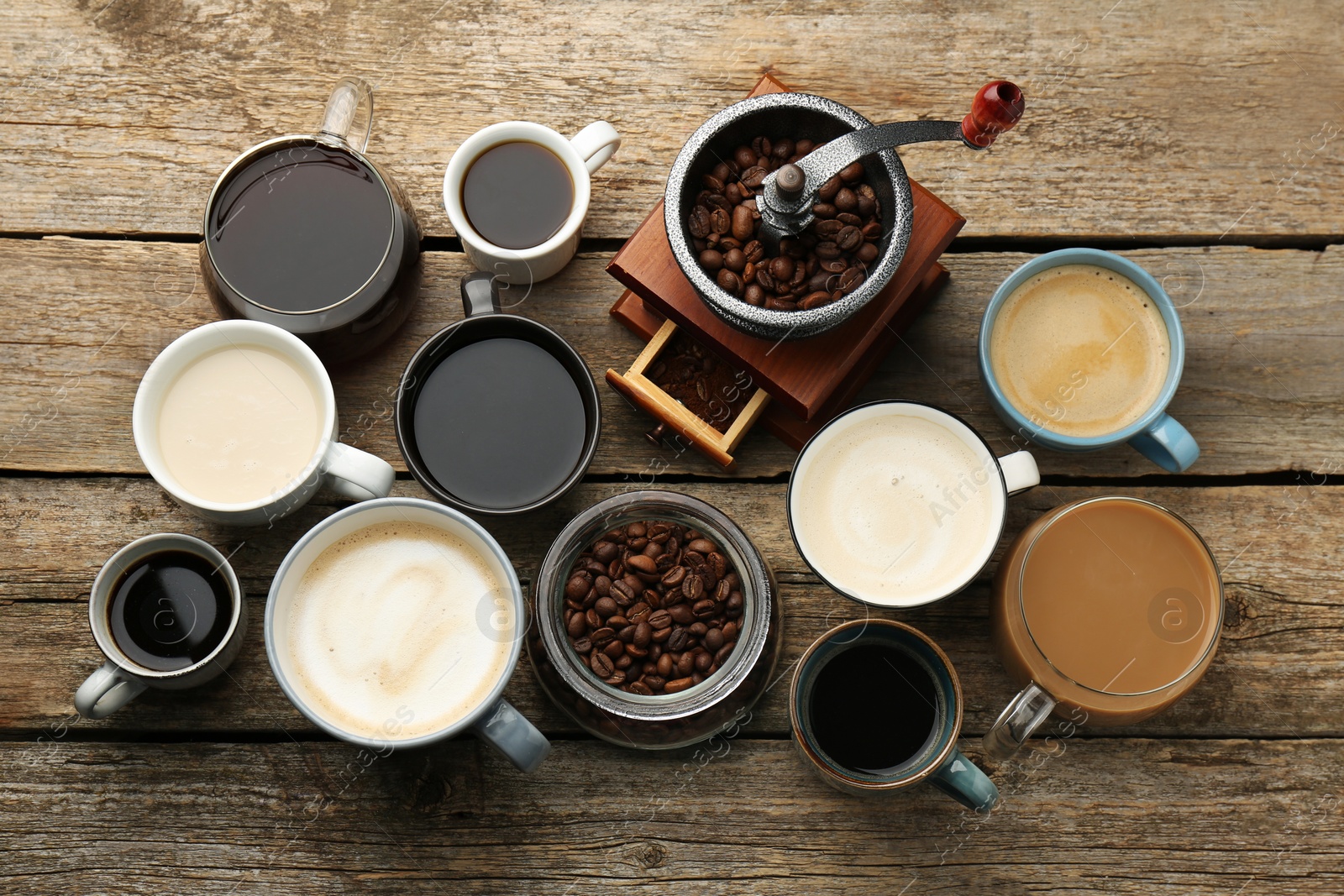 Photo of Different coffee drinks in cups, beans and manual grinder on wooden table, flat lay