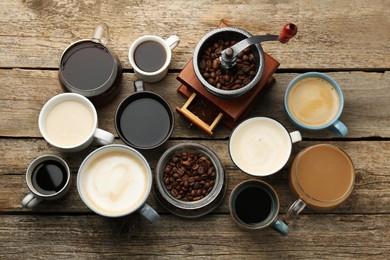 Different coffee drinks in cups, beans and manual grinder on wooden table, flat lay