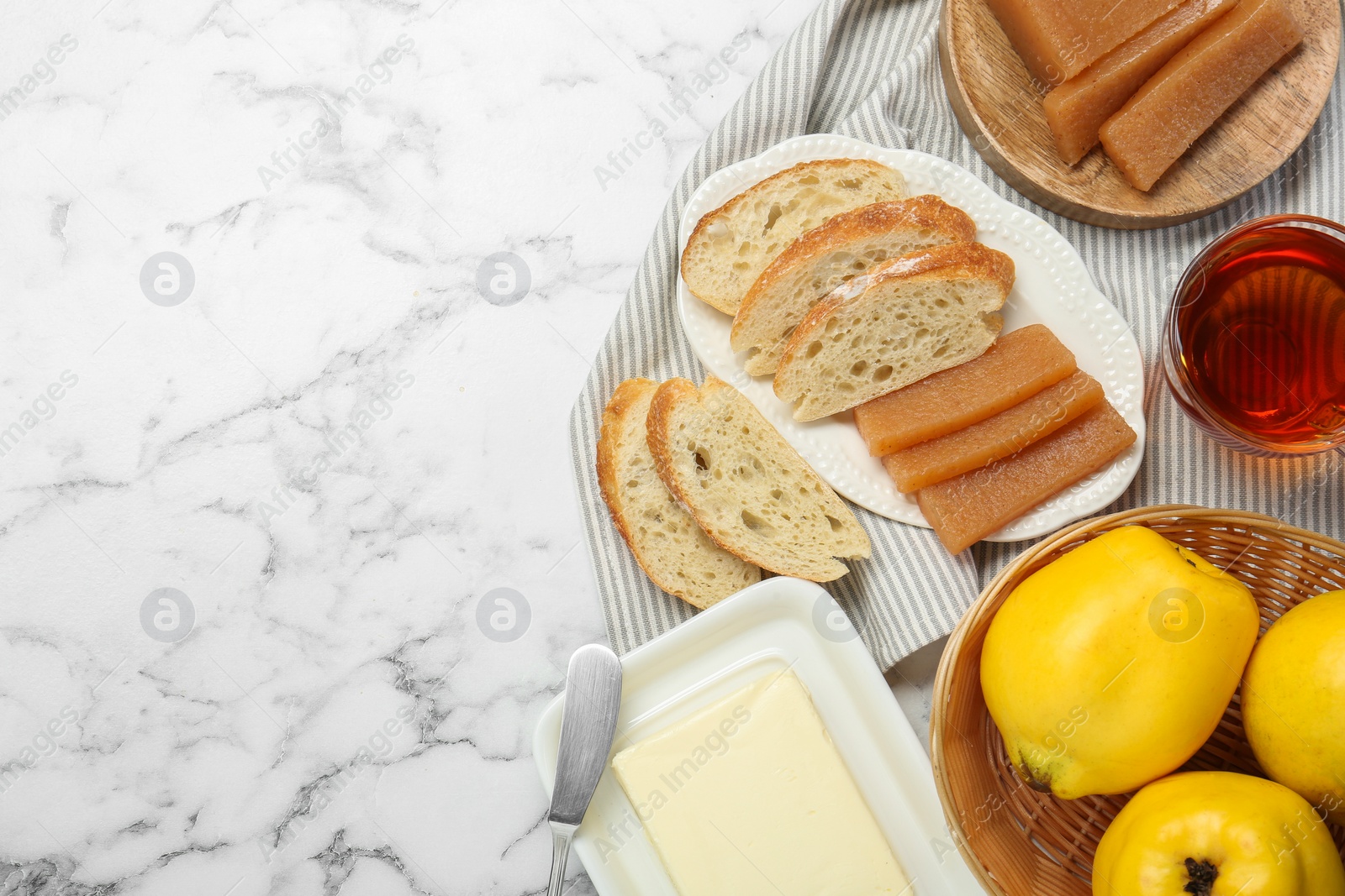 Photo of Delicious quince paste, bread, butter, cup of tea and fresh fruits on white marble table, flat lay. Space for text