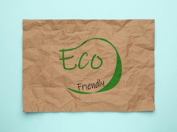 Sheet of crumpled paper with phrase Eco Friendly on light blue background, top view