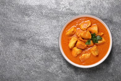 Photo of Bowl of delicious chicken curry on grey table, top view. Space for text