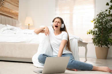 Lazy young woman with laptop and headphones in bedroom