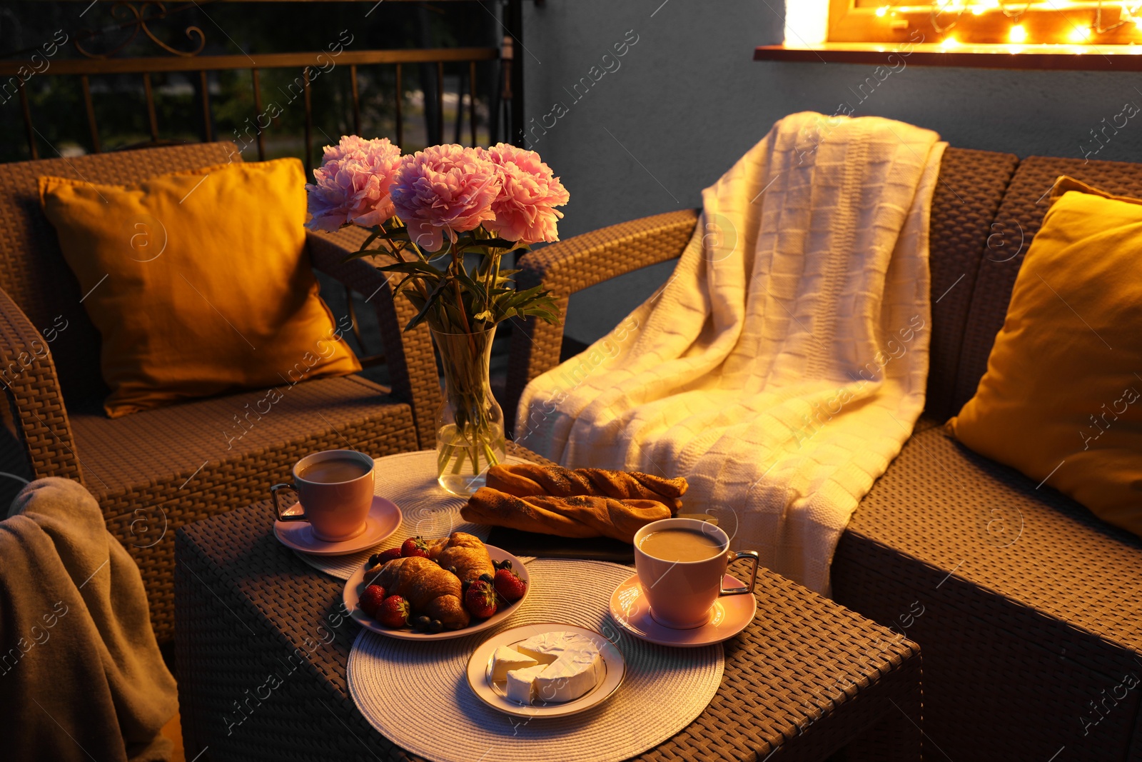 Photo of Rattan table with drink, food and flowers on outdoor terrace in evening