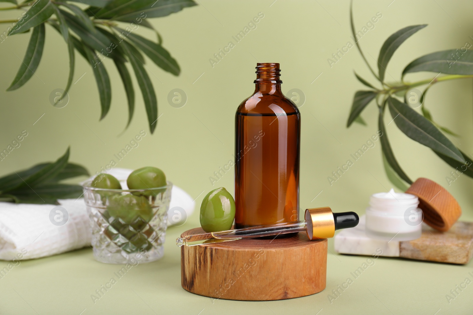 Photo of Glass bottle of serum and olives on green background