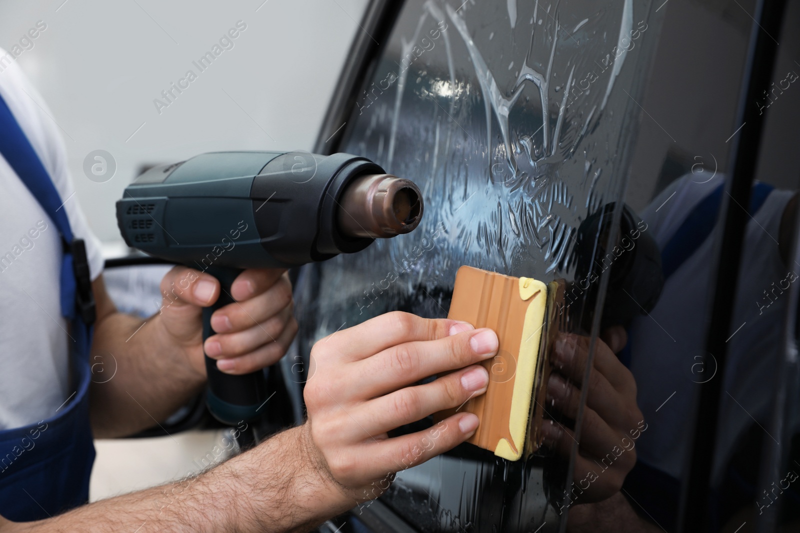 Photo of Worker tinting car window with foil in workshop, closeup