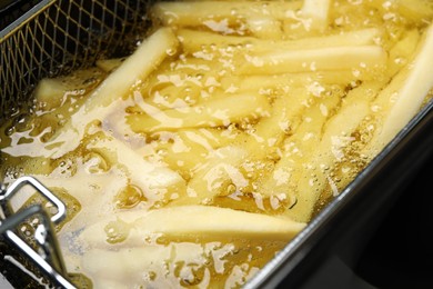 Photo of Cooking delicious french fries in hot oil, closeup