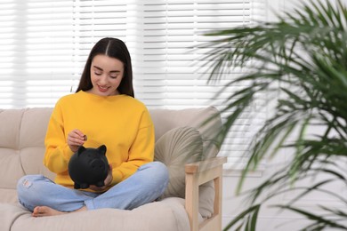 Young woman putting coin into piggy bank at home