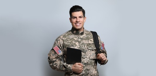 Military education. Cadet with backpack and tablet on light grey background