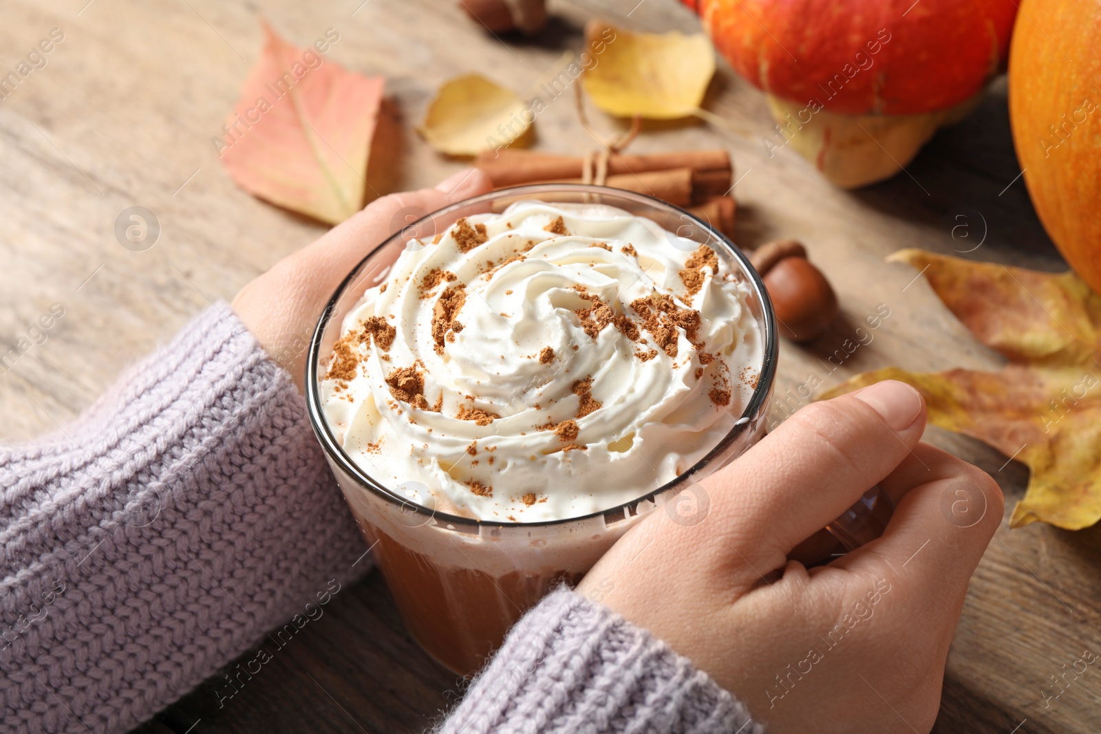 Photo of Woman holding glass cup of tasty pumpkin spice latte at wooden table, closeup