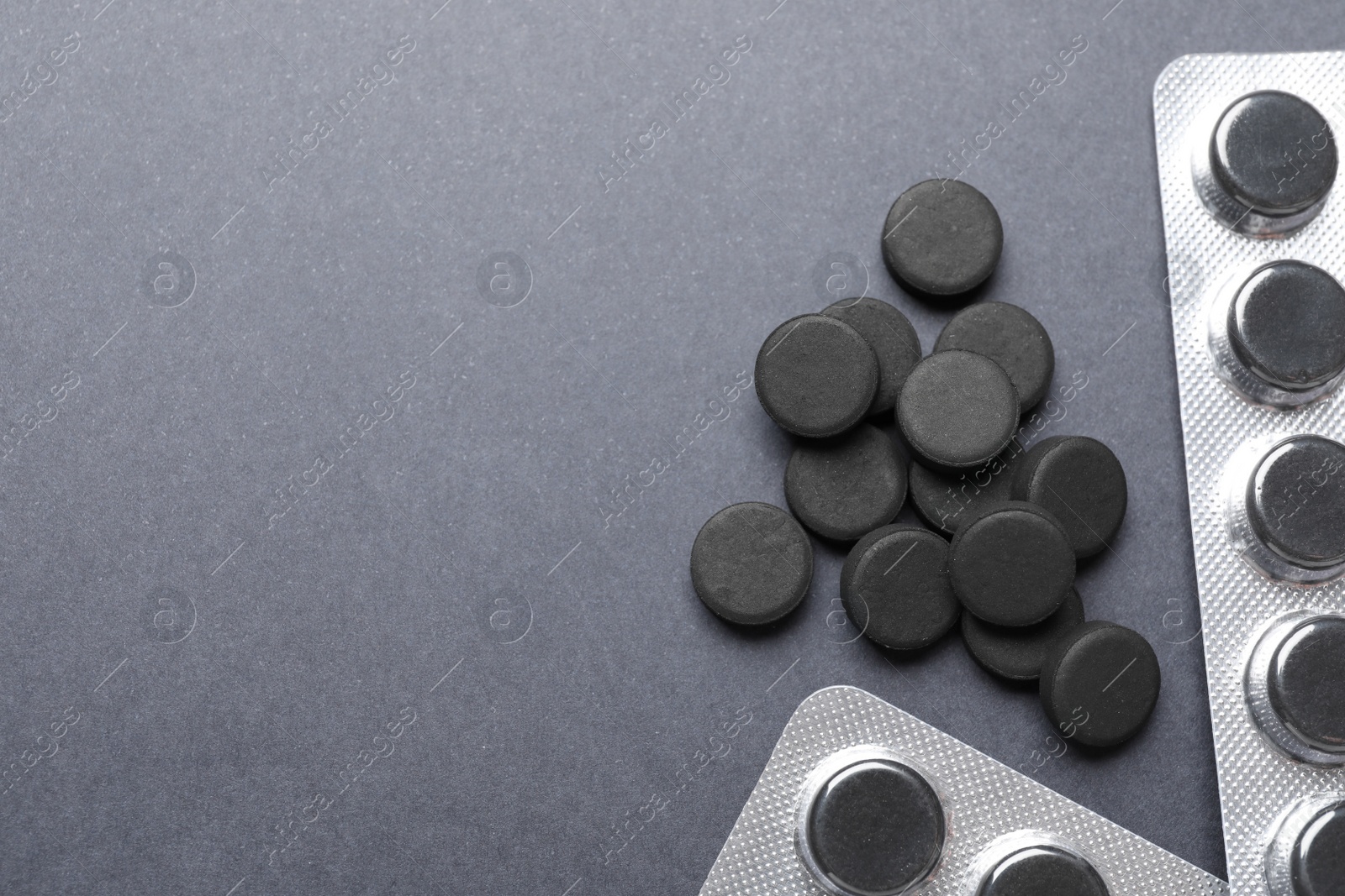 Photo of Activated charcoal pills on grey background, flat lay with space for text. Potent sorbent