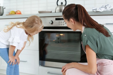 Photo of Young woman and her daughter baking something in oven at home