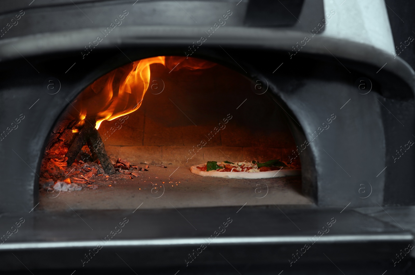 Photo of Burning firewood and tasty pizza in oven at restaurant kitchen