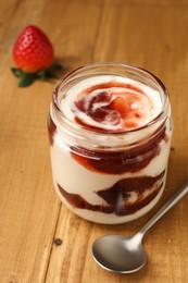 Photo of Tasty yoghurt with jam, spoon and strawberry on wooden table, closeup