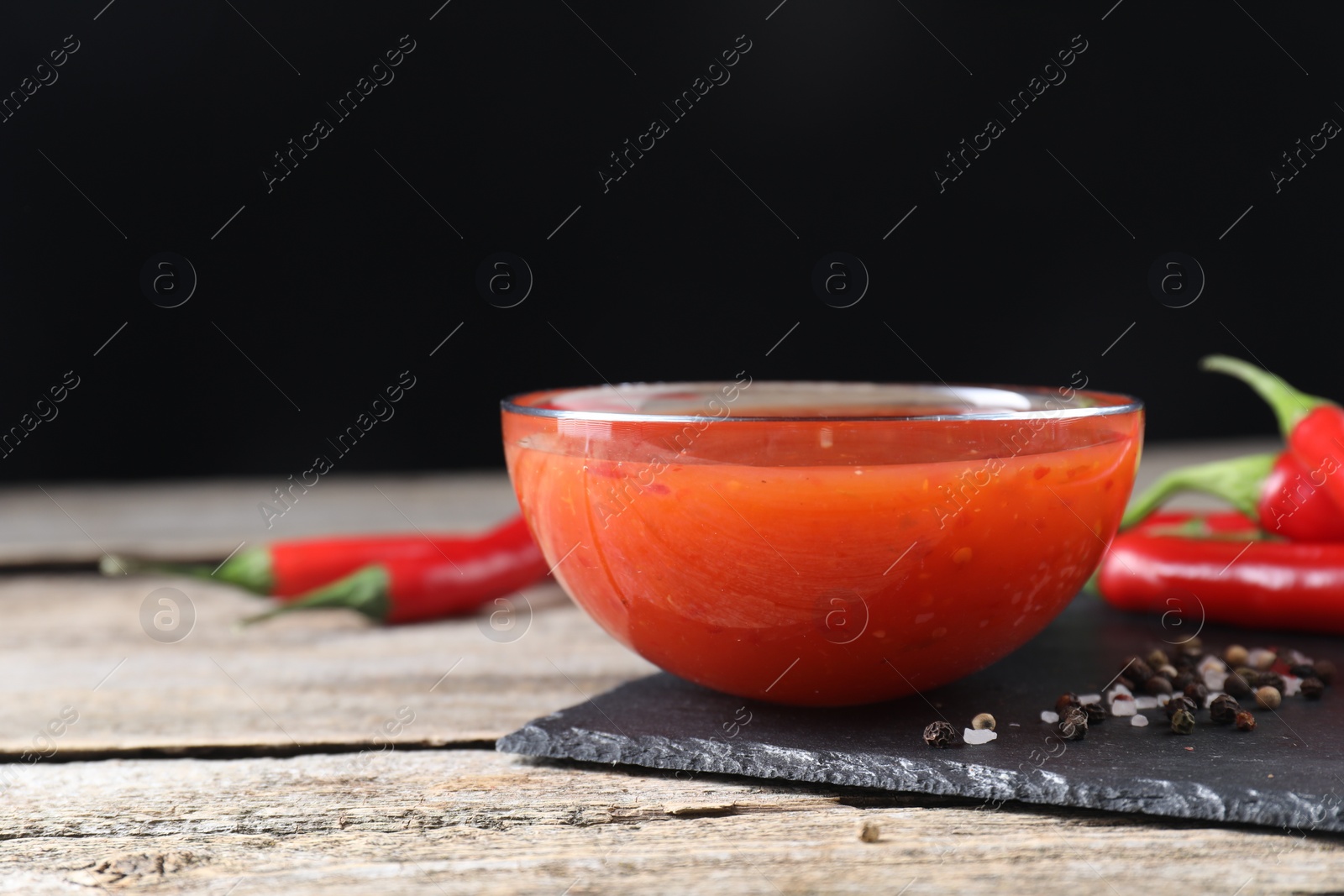 Photo of Spicy chili sauce in bowl on wooden table. Space for text