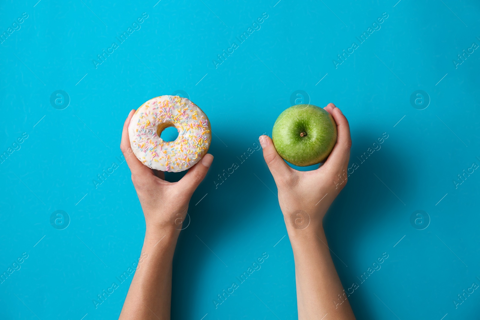 Photo of Choice concept. Top view of woman with doughnut and apple on light blue background, closeup