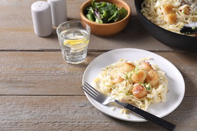 Photo of Delicious scallop pasta with onion served on wooden table, space for text