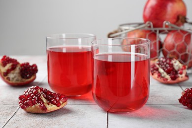 Photo of Tasty pomegranate juice in glasses and fresh fruits on white tiled table