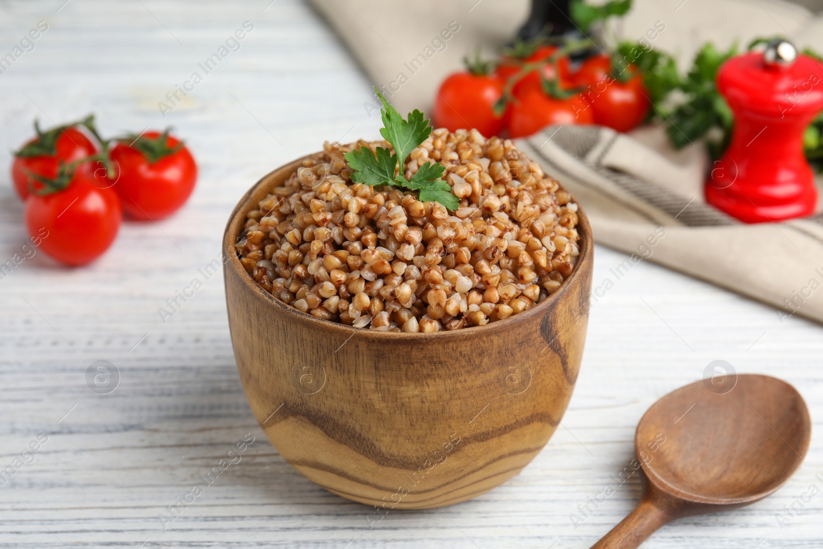 Photo of Bowl of buckwheat porridge with parsley served on white wooden table