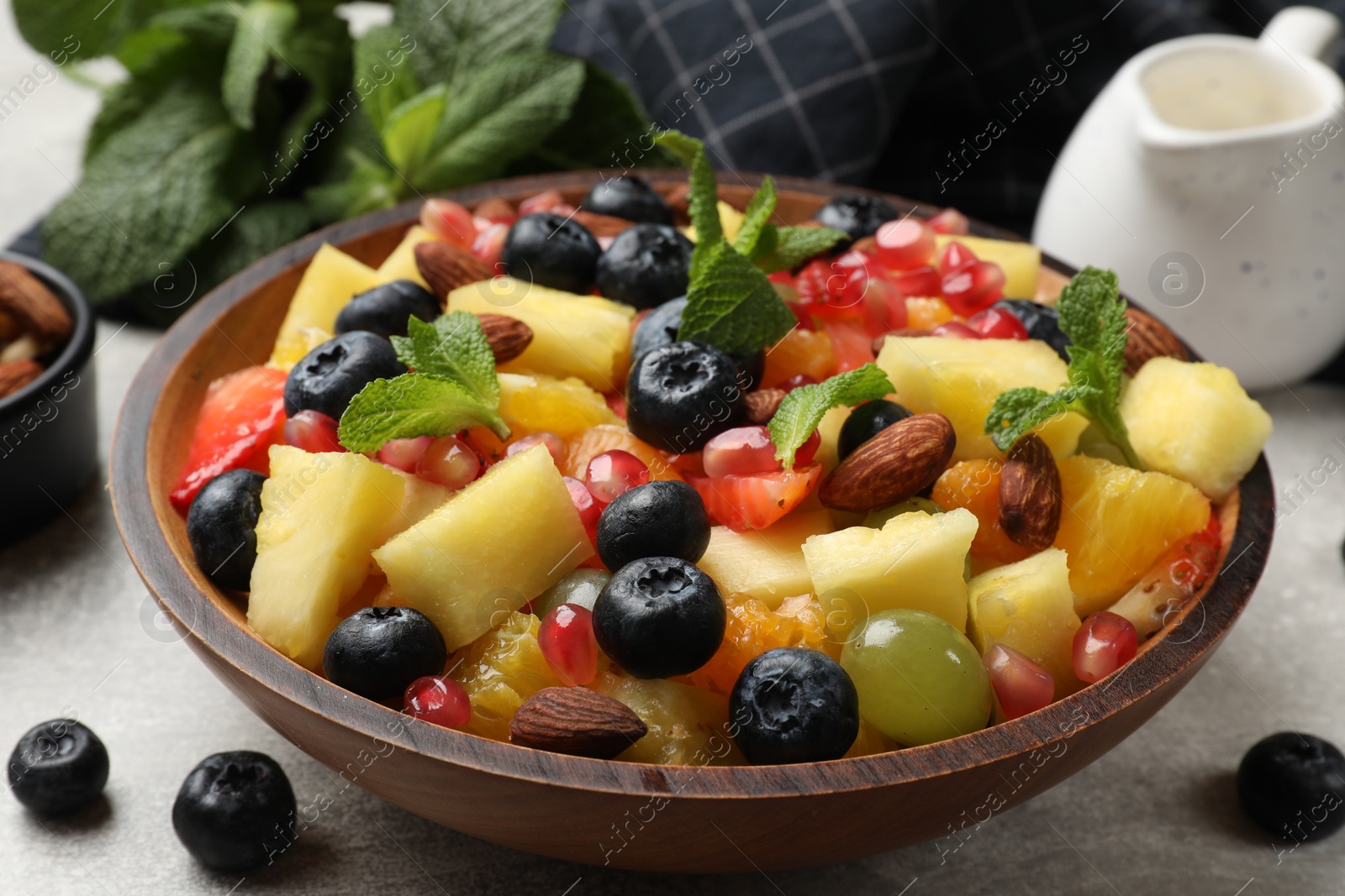 Photo of Delicious fruit salad in bowl, berries, nuts and fresh mint on grey table