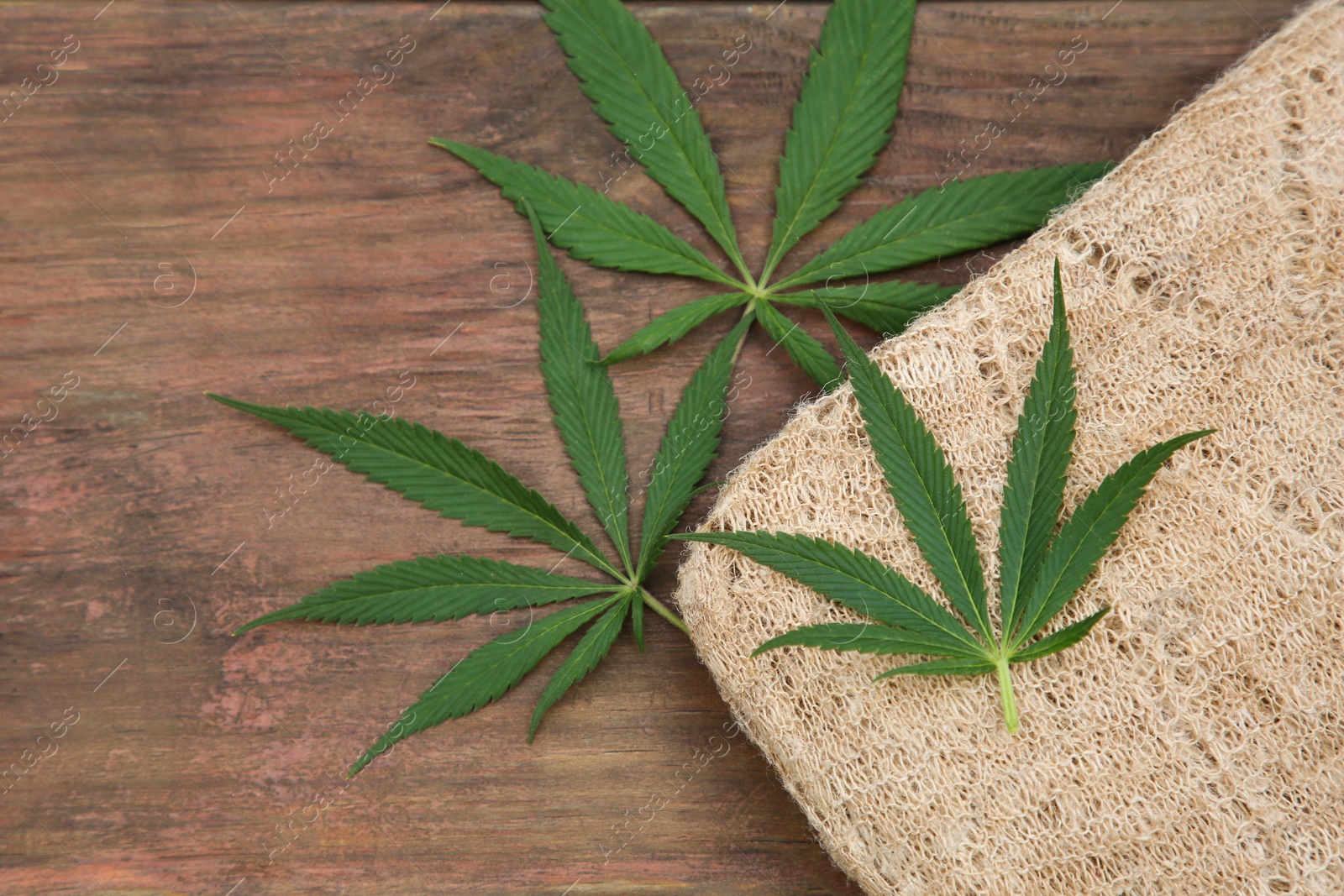 Photo of Hemp cloth and green leaves on wooden table, flat lay