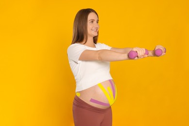Pregnant woman with kinesio tapes on her belly doing exercises against orange background