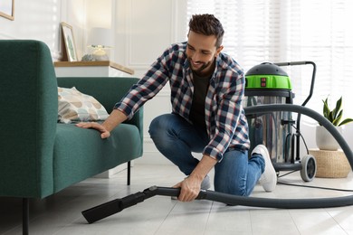 Man vacuuming floor under sofa in living room