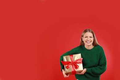 Happy young woman with Christmas gift on red background. Space for text