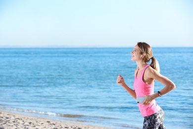 Photo of Young woman listening to music and running on beach in morning