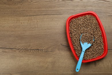 Photo of Cat litter tray with filler and scoop on wooden floor, top view. Space for text