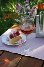 Photo of Vase with spring flowers, wine and cake on table served for romantic date in garden