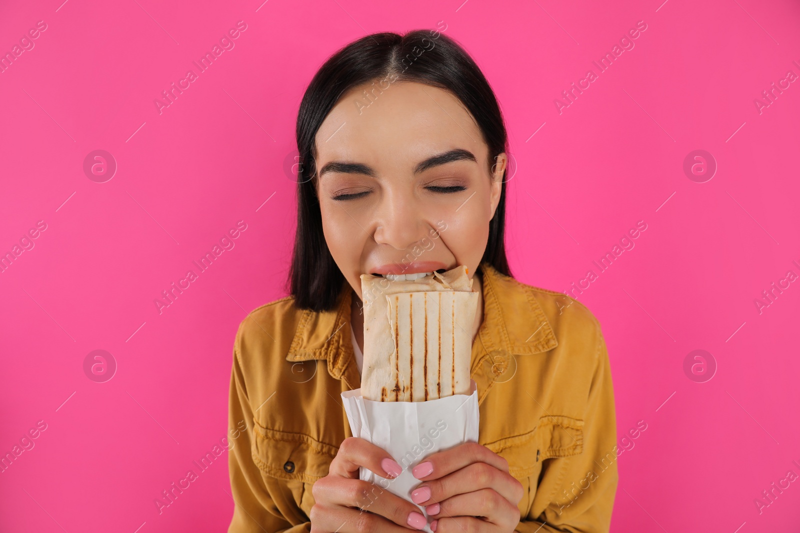 Photo of Young woman eating delicious shawarma on pink background