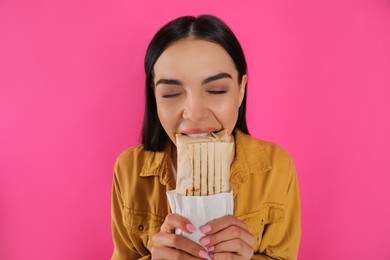 Young woman eating delicious shawarma on pink background