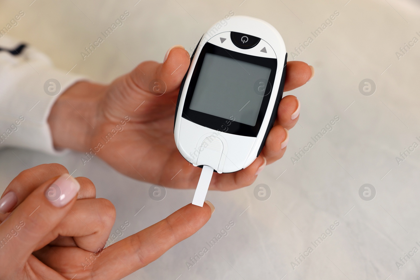 Photo of Diabetes. Woman checking blood sugar level with glucometer at light table, closeup