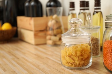 Photo of Glass jar with pasta on wooden countertop in kitchen, space for text