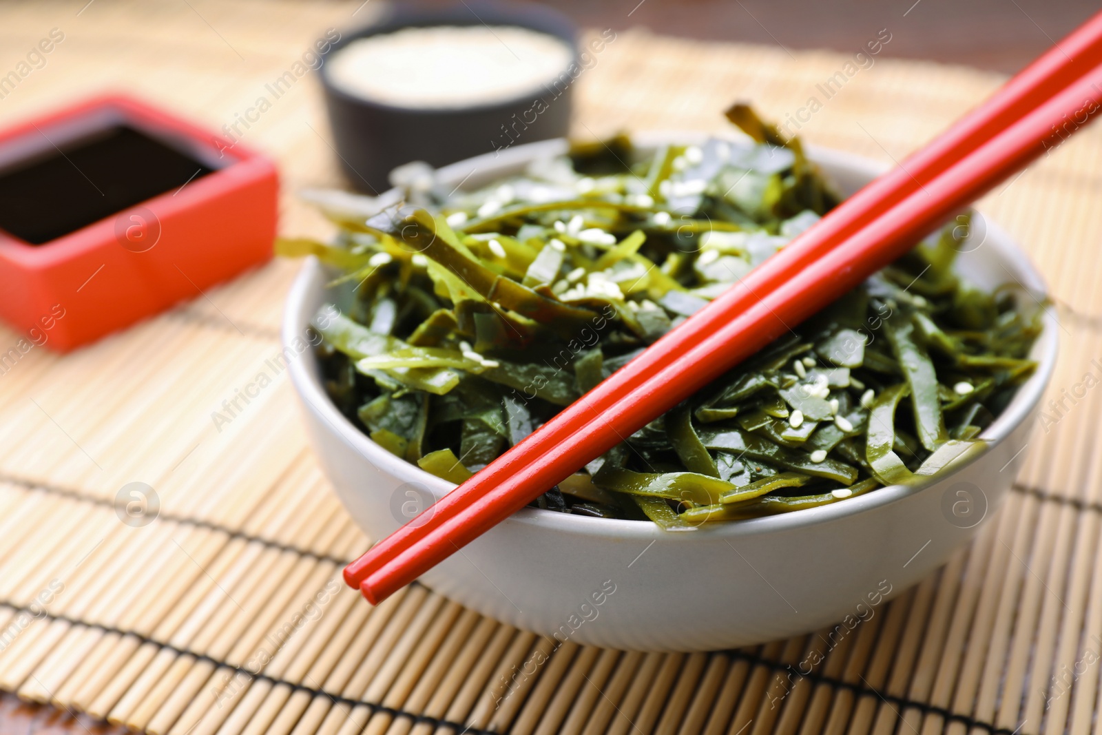 Photo of Fresh laminaria (kelp) seaweed in bowl and chopsticks on table, closeup