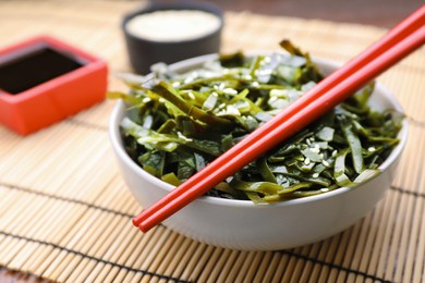 Photo of Fresh laminaria (kelp) seaweed in bowl and chopsticks on table, closeup