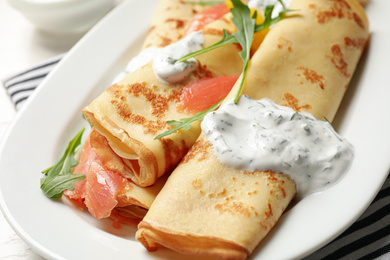 Delicious thin pancakes with salmon and sour cream on plate, closeup