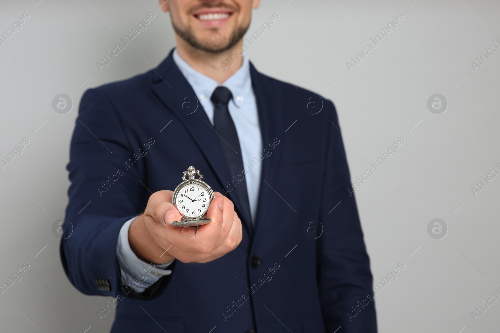 Photo of Happy businessman holding pocket watch on grey background, closeup. Time management